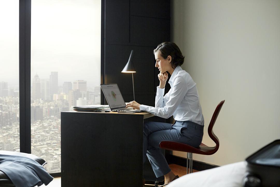 Mulher trabalhando em notebook em mesa próxima à janela, ilustrando práticas de ergonomia no trabalho em home office.